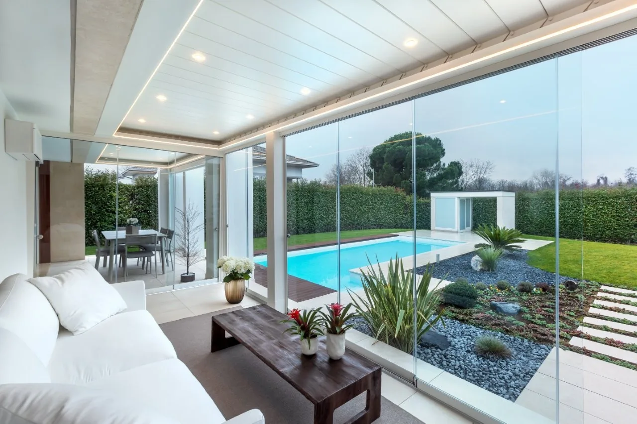 Salotto affacciato sulla piscina attraverso le vetrate della pergola ECCELSA